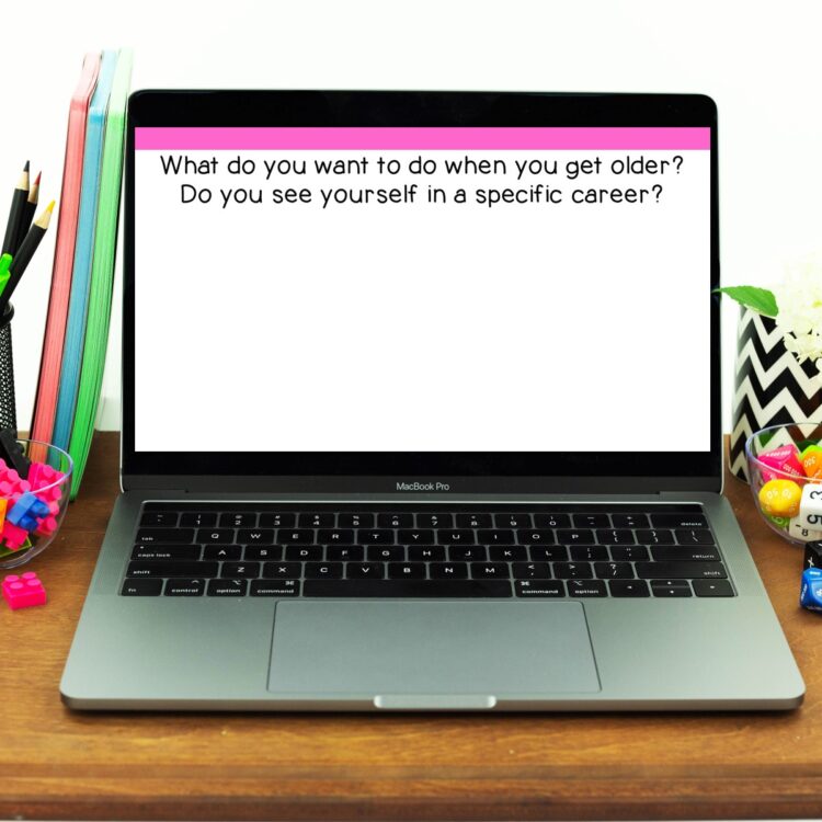 Writing prompt about career on a laptop screen. Laptop is sitting on a desk with various school supplies around it