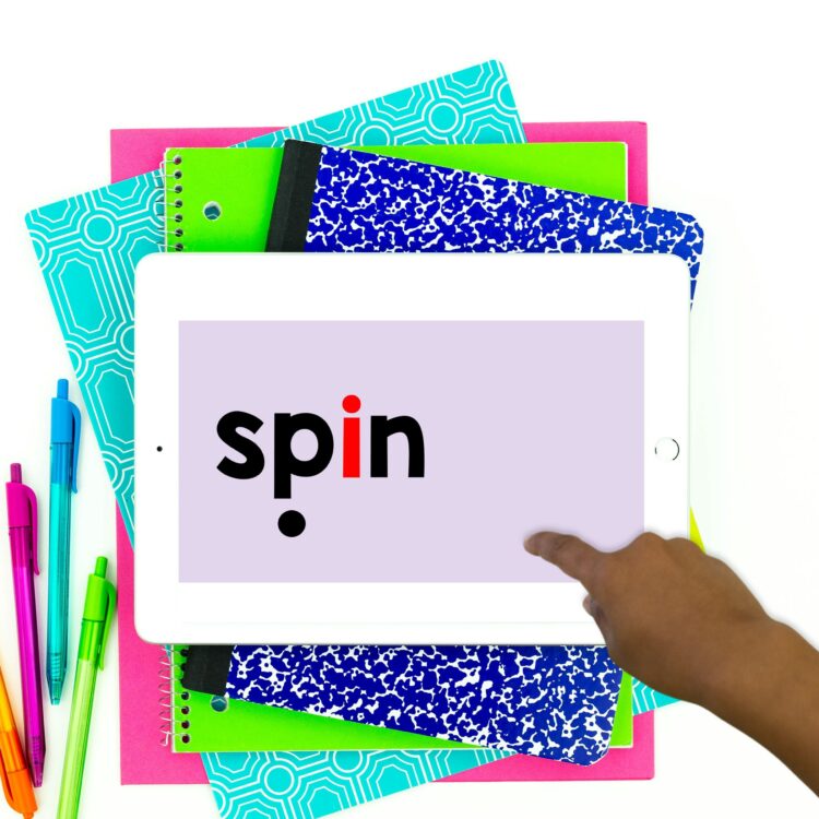 "spin" with a visual cue for successive blending displayed on an ipad atop a stack of books. It appears that a Black student is tapping to advance the slide. 